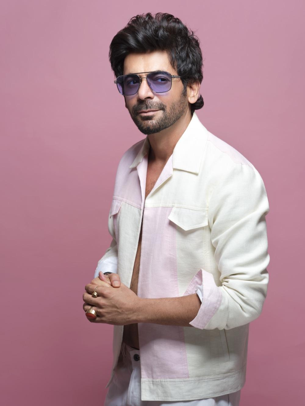 Sunil Grover in tinted sunglasses and a pale jacket on a pink backdrop