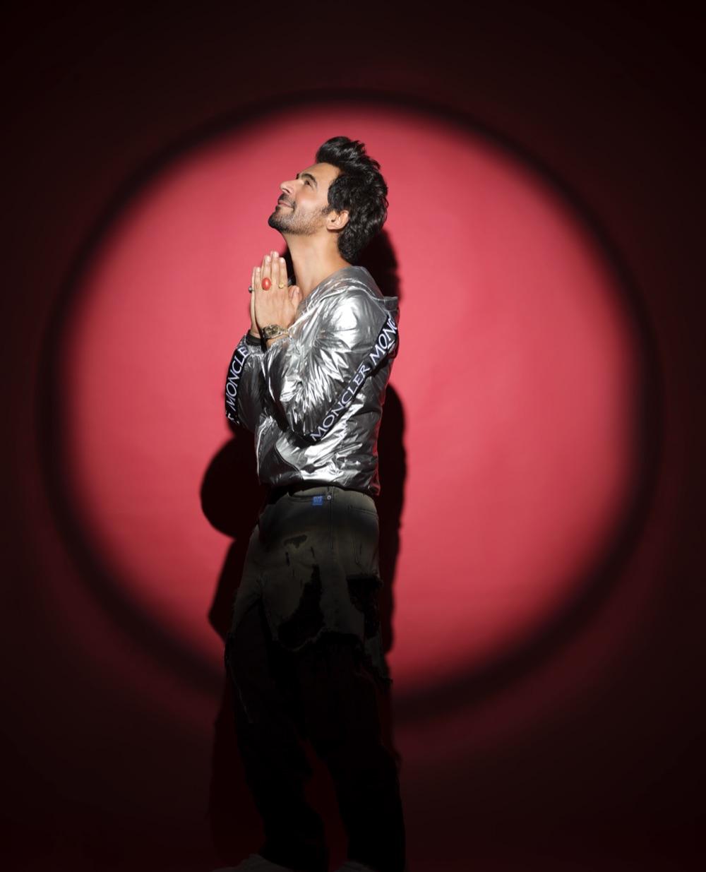 Sunil Grover looking upward with hands together, lit by a red spotlight