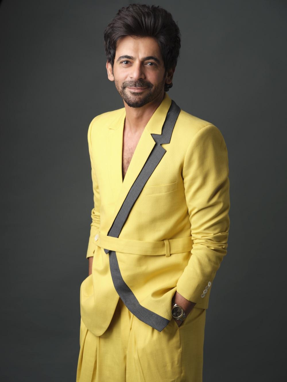 Sunil Grover in a bright yellow suit against a grey studio backdrop